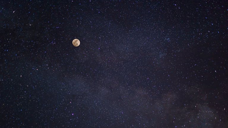 A breathtaking view of the full moon against a starry night sky with the Milky Way.