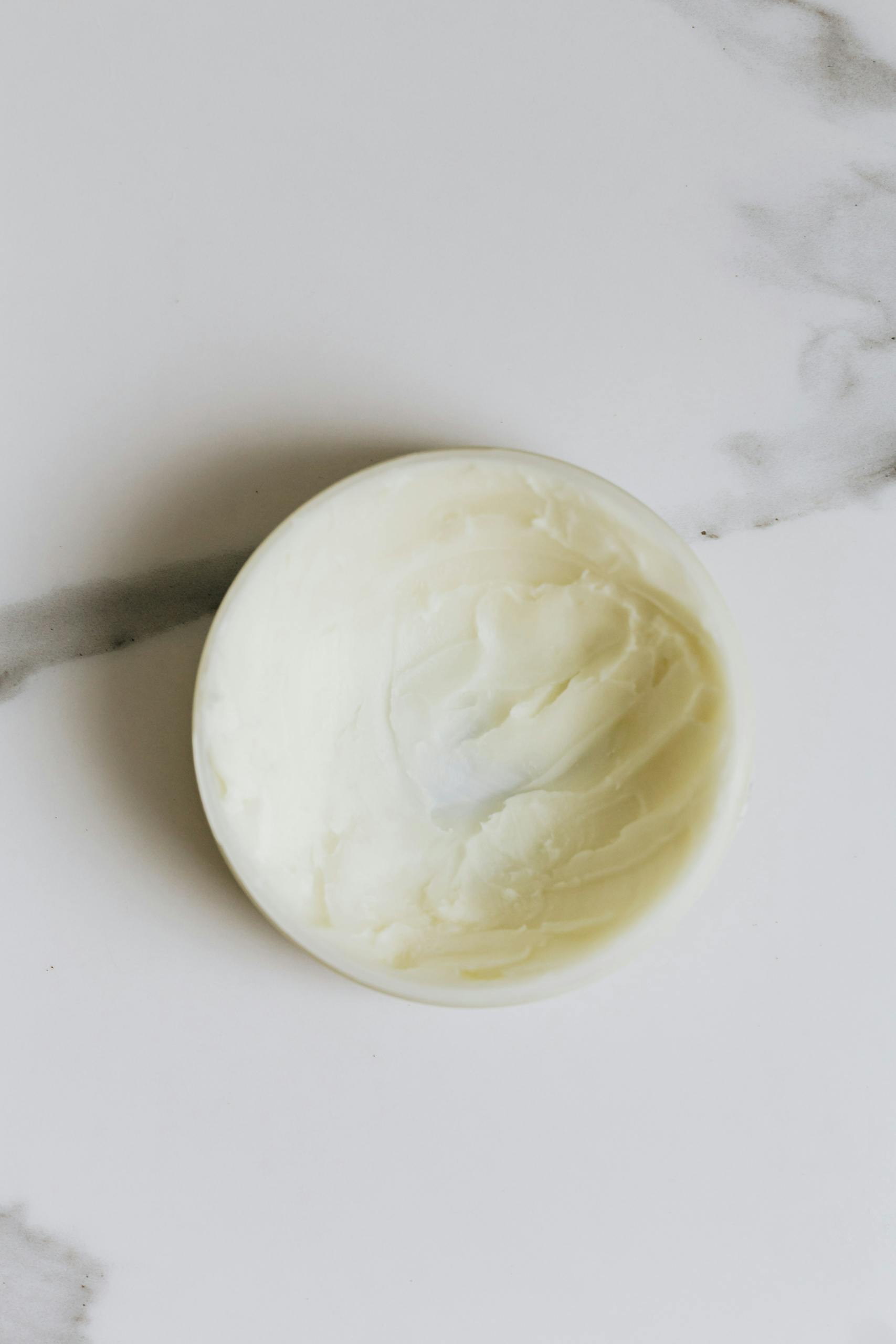 Creamy skincare product in round container on marble surface.