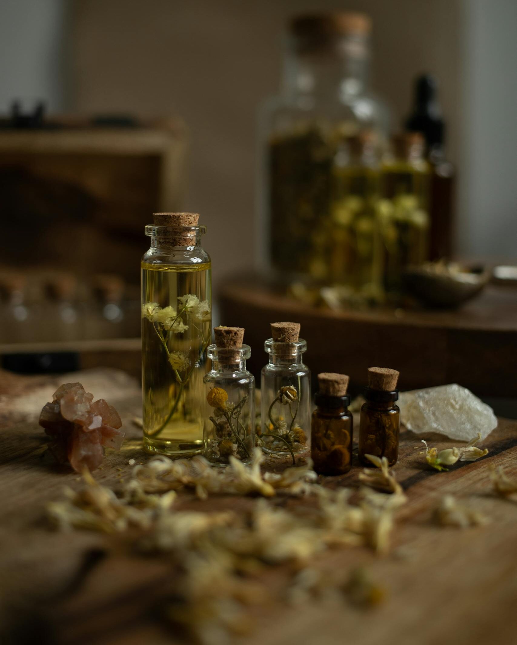 Rustikk samling av glassflasker med essensielle oljer og aromatiske urter på trebord for aromaterapi.