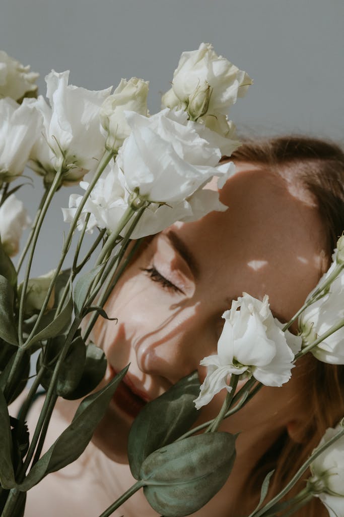 A serene portrait of a woman with closed eyes among beautiful white roses in gentle lighting.